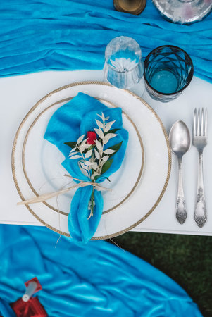 White banquet table covered with blue cloth, served with plates, cutlery, glasses, candles and flower arrangements. Top view. Copy, empty space for text.の写真素材