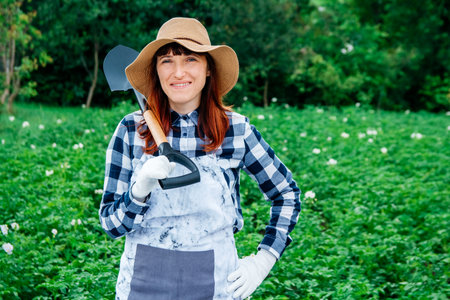 Portrait of a beautiful woman farmer holds a bunch of carrots in a straw hat and surrounded by the many plants in her vegetable garden.の写真素材