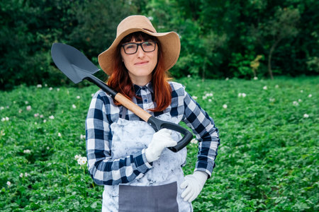 Portrait of a beautiful woman farmer holds a bunch of carrots in a straw hat and surrounded by the many plants in her vegetable garden.の写真素材