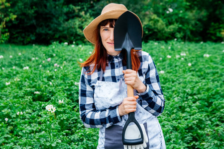 Portrait of a beautiful woman farmer holds a bunch of carrots in a straw hat and surrounded by the many plants in her vegetable garden.の写真素材