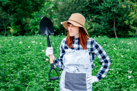Portrait of a beautiful woman farmer holds a bunch of carrots in a straw hat and surrounded by the many plants in her vegetable garden.の写真素材
