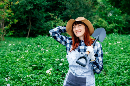 Portrait of a beautiful woman farmer holds a bunch of carrots in a straw hat and surrounded by the many plants in her vegetable garden.の写真素材