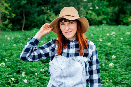 Portrait beautiful female farmer smiling at the camera wearing a straw hat and surrounded by the many plants in her vegetable garden.の写真素材