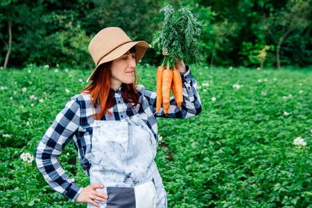 Portrait beautiful female farmer smiling at the camera wearing a straw hat and surrounded by the many plants in her vegetable garden.の写真素材