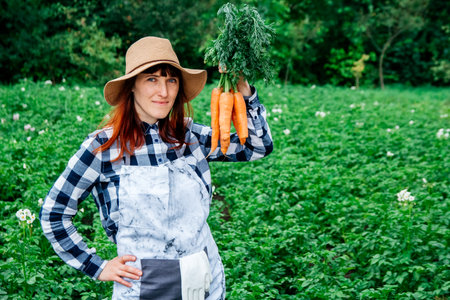 Portrait beautiful female farmer smiling at the camera wearing a straw hat and surrounded by the many plants in her vegetable garden.の写真素材