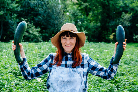 Portrait beautiful female farmer smiling at the camera wearing a straw hat and surrounded by the many plants in her vegetable garden.の写真素材