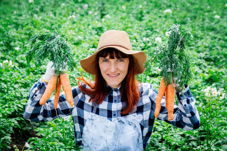 Portrait beautiful female farmer smiling at the camera wearing a straw hat and surrounded by the many plants in her vegetable garden.の写真素材