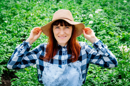 Portrait beautiful female farmer smiling at the camera wearing a straw hat and surrounded by the many plants in her vegetable garden.の写真素材