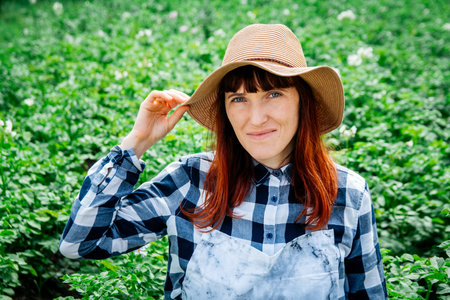 Portrait of a beautiful woman farmer holds a bunch of carrots in a straw hat and surrounded by the many plants in her vegetable garden.の写真素材