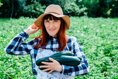 Portrait of a beautiful woman farmer holds a bunch of carrots in a straw hat and surrounded by the many plants in her vegetable garden.の写真素材