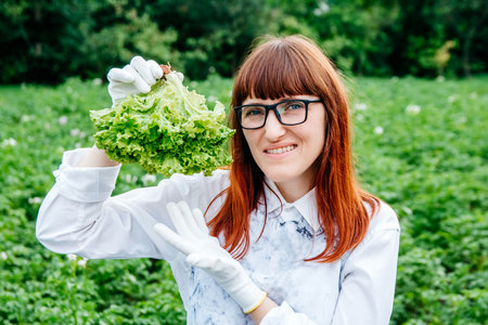Beautiful female farmer holding green cabbage leaves in wicker basket, smiling at the camera and surrounded by plenty of plants in her vegetable garden.の写真素材