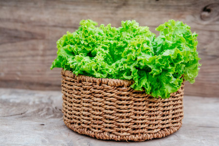 Close up of green leaves of kale in a wicker basket on a wooden background.の写真素材