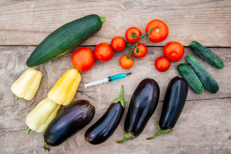 Vegetables and syringe with blue liquid on wooden background. Concept of Non-natural Products, Gmo.の写真素材