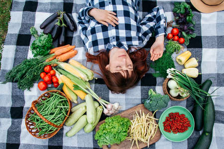 Portrait beautiful woman farmer with closed eyes lying on a plaid among fresh organic vegetables. Top view.の写真素材
