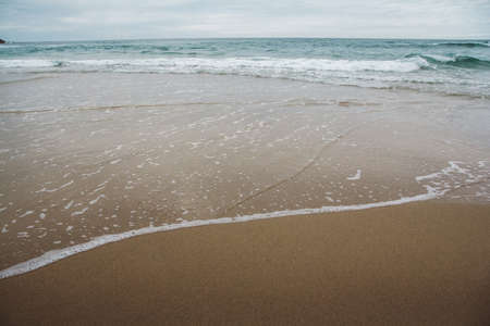 Ocean waves on a sandy beach with cloudy skiesの写真素材