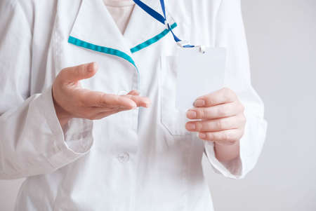 Woman doctor in a white coat holding a empty blank badgeの写真素材