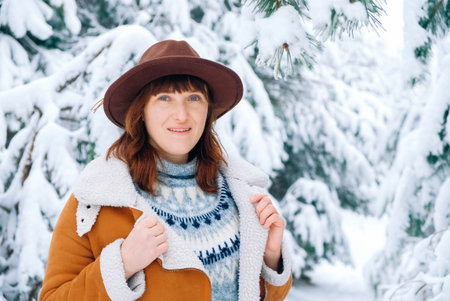 Young woman wearing hat and warm jacket standing among snowy trees and enjoying first snow.