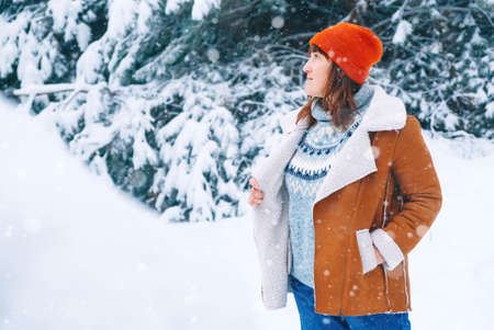 Winter portrait of woman in a red warm hat and jacket standing on a background of snowy forest. Copy, empty space for text.の写真素材