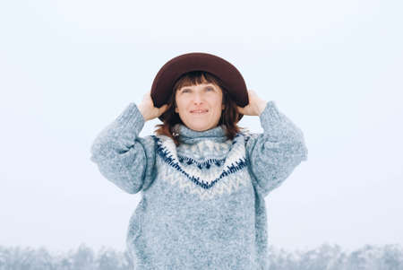 Woman in a brown hat and sweater on a background of snow-covered forest.の写真素材