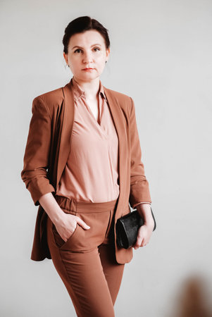 Woman dressed in a brown business suit with a black handbag on a white background. Copy, empty spaceの写真素材