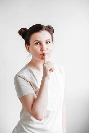 Portrait woman with pigtails holding forefinger on her lips while standing over white backgrounnd. Copy, empty spaceの写真素材