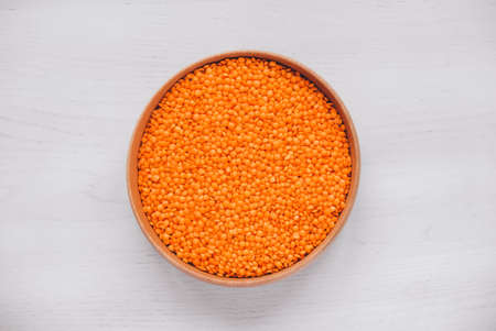 Raw red lentils in a wooden bowl on a white table.の写真素材