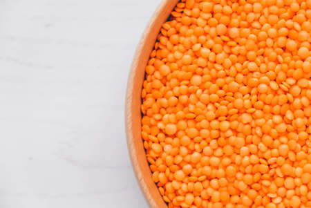 Raw red lentils in a wooden bowl on a white table.の写真素材