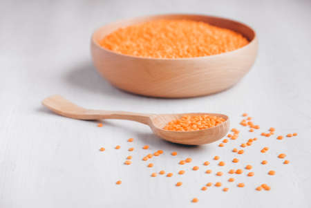 Raw red lentils in a wooden bowl and spoon on a white table.の写真素材
