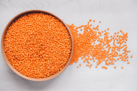 Raw red lentils in a wooden bowl on a white table.