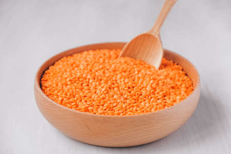 Raw red lentils in a wooden bowl and spoon on a white table.の写真素材