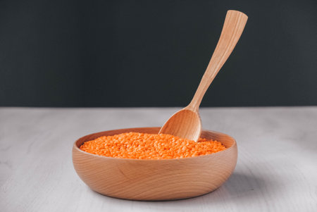 Raw red lentils in a wooden bowl and spoon on a white table.