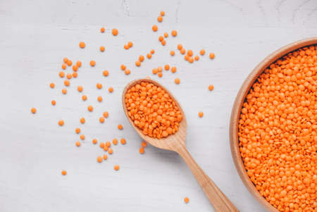 Raw red lentils in a wooden bowl and spoon on a white table.の写真素材