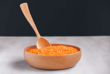 Raw red lentils in a wooden bowl and spoon on a white table.の写真素材