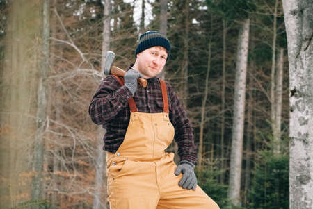 Portrait of a man lumberjack with an ax in his hands on a background of forest and treesの写真素材