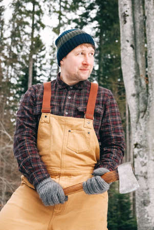 Portrait of a man lumberjack with an ax in his hands on a background of forest and treesの写真素材