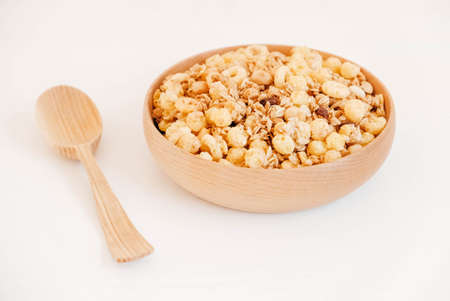 Dry muesli with cornflakes, nuts and raisins in a wooden bowl on a white background.の写真素材