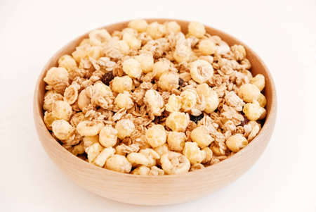 Dry muesli with cornflakes, nuts and raisins in a wooden bowl on a white background.の写真素材