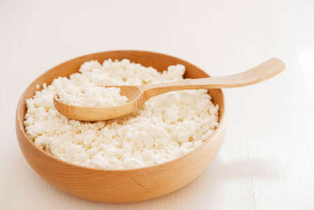 Cottage cheese in a wooden plate with a spoon on a white background.の写真素材