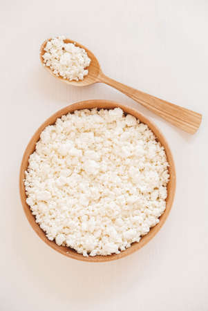 Cottage cheese in a wooden plate with a spoon on a white backgroundの写真素材