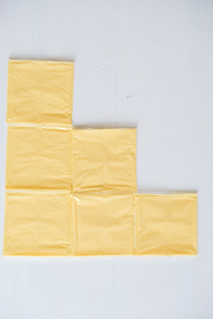 Separately packed cheese slices on a white wooden table background
