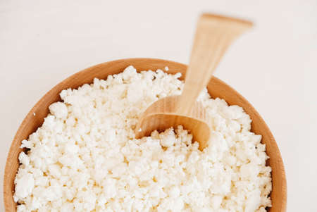 Cottage cheese in a wooden plate with a spoon on a white backgroundの写真素材