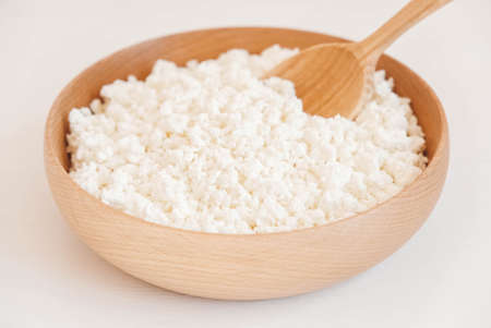Cottage cheese in a wooden plate with a spoon on a white backgroundの写真素材