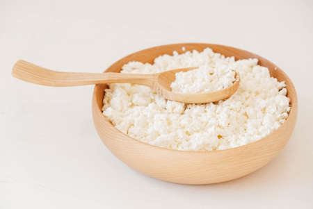 Cottage cheese in a wooden plate with a spoon on a white backgroundの写真素材