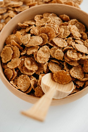 Crispy healthy dry cereal flakes in a wooden bowl with wooden spoon on white background.