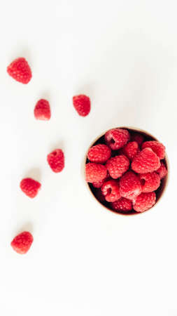 Fresh red raspberries in a paper cup on a white table background.の写真素材