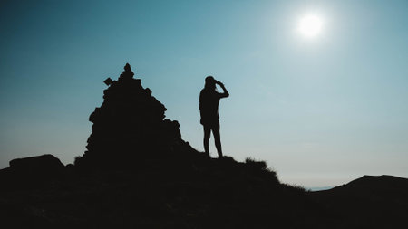 Silhouette of woman standing on rock near the edge of mountain on background of sky.