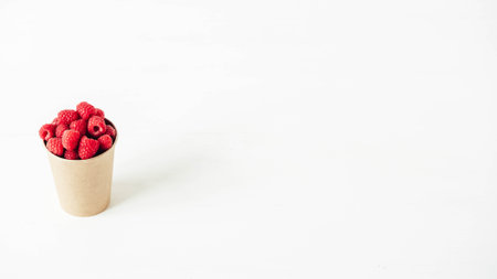 Fresh red raspberries in a paper cup on a white table background.の写真素材