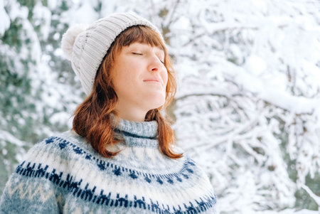 Winter portrait of a woman in a warm hat and sweater on a background of snowy forest.