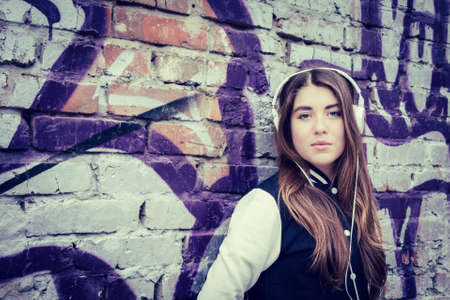 Teenage girl  with headphones posing near graffiti wallの写真素材