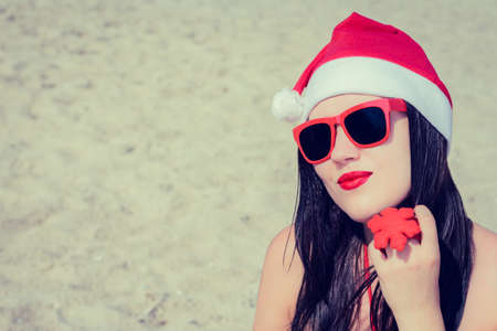 Portrait of a smiling young woman  in Santa Claus hat and sunglasses on a beach. Toned effectの写真素材